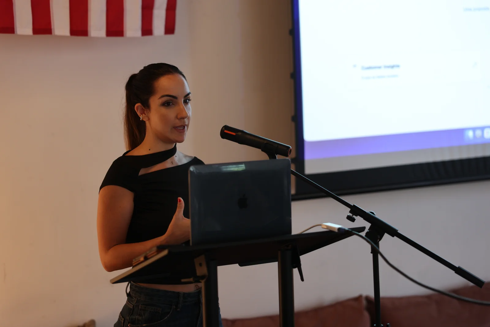 A presenter speaking into a microphone beside a projected demo at Fractal Campus